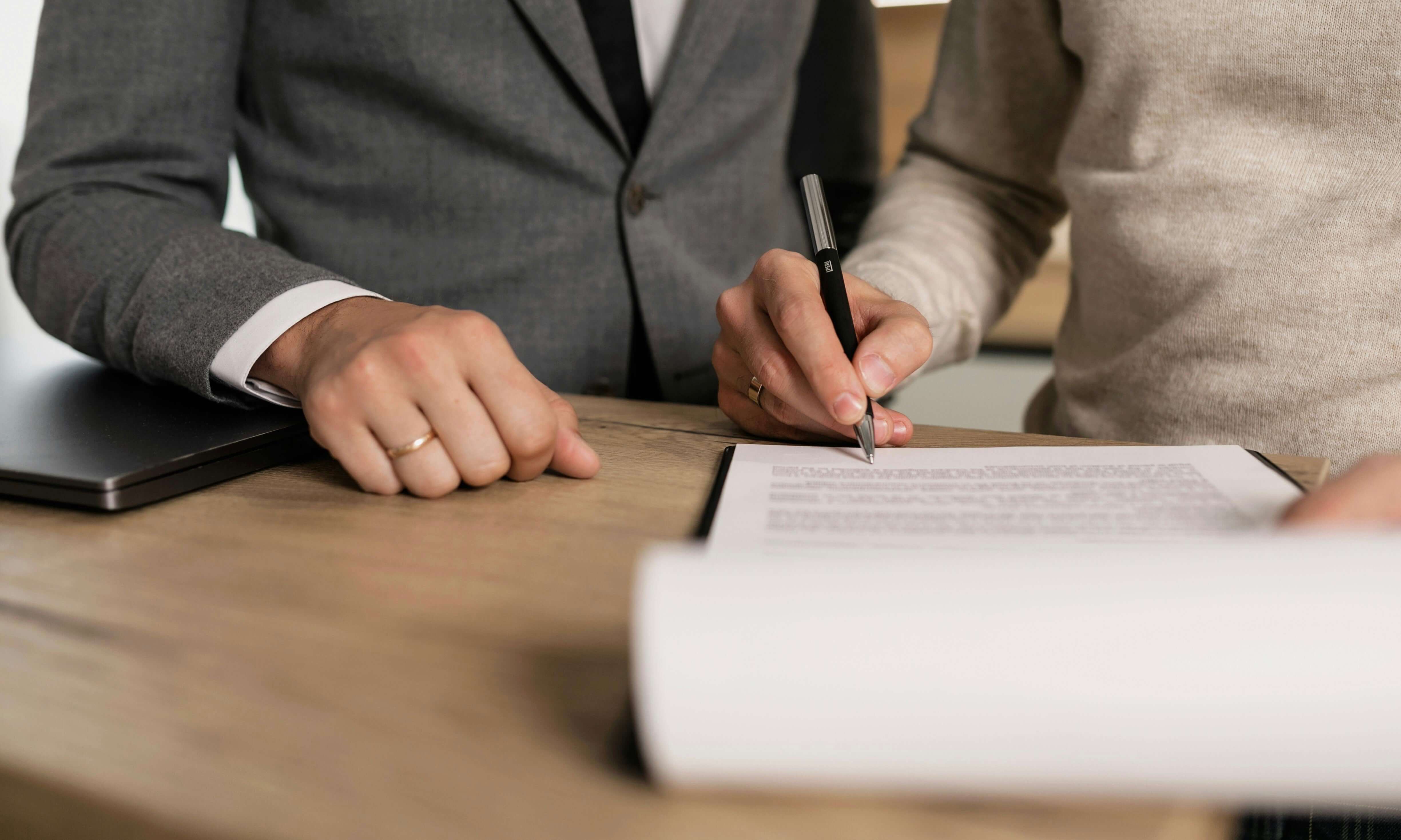 Professional legal consultation - hands signing legal documents at a wooden table